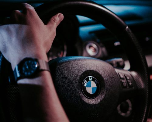 Close-up of a hand on a BMW steering wheel at night, showcasing the car interior.